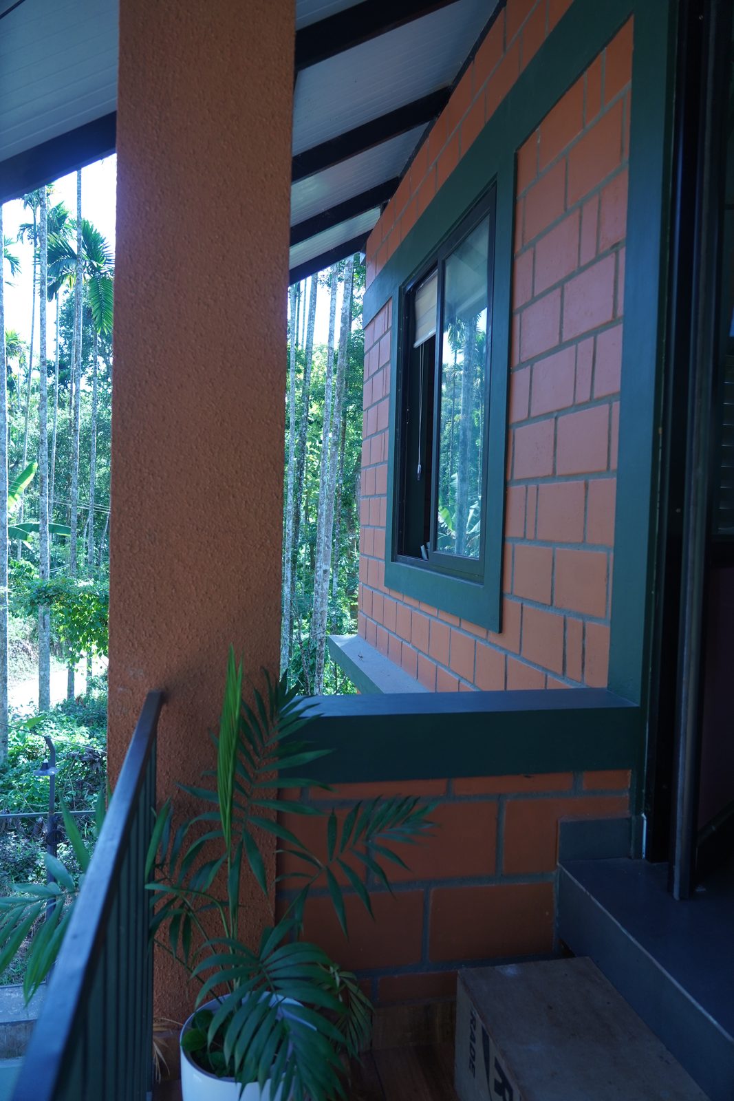 Balcony corner with a terracotta brick wall, a window and tall areca palms beyond