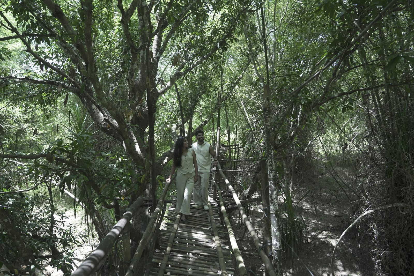 A couple walking along a wooden bamboo walkway through the forest