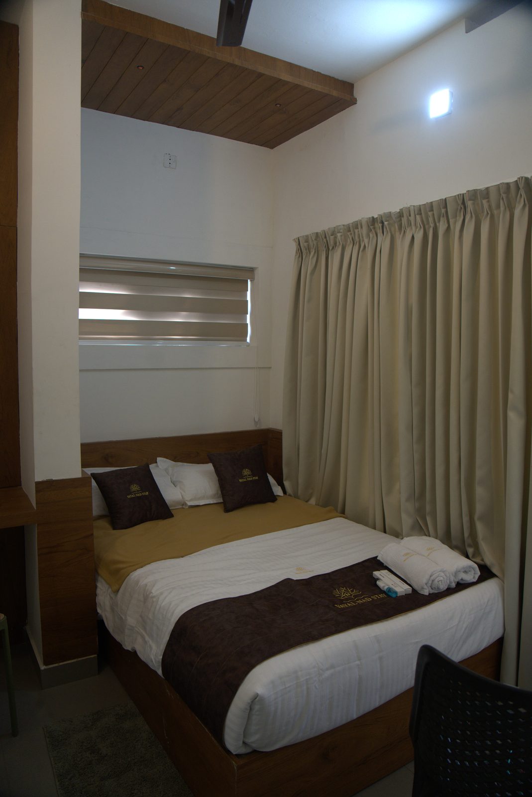 Made-up bed with a folded towel, a wooden headboard and curtains
