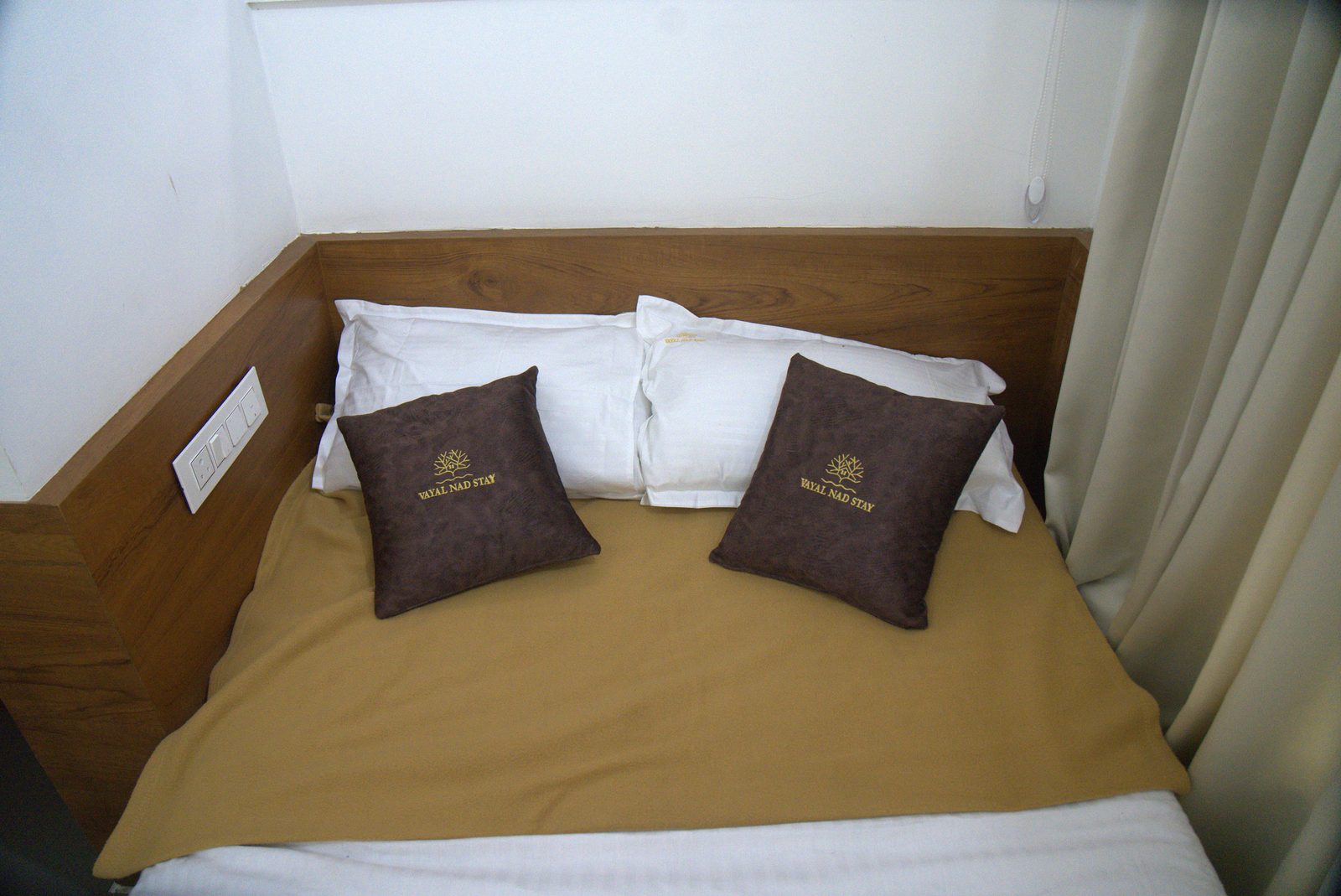 Bed with branded pillows, a wooden headboard and cream curtains