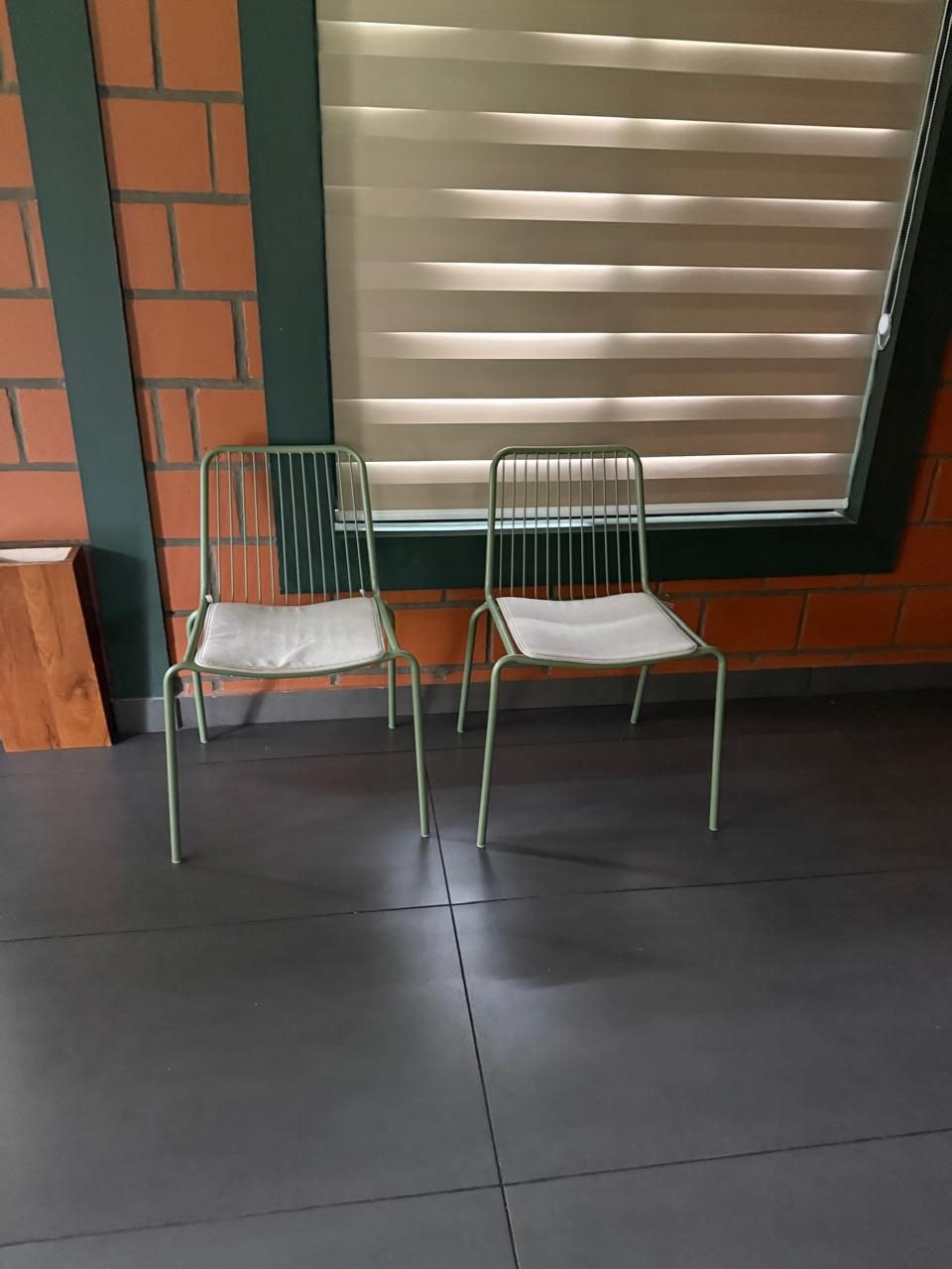 Two green metal chairs against an exposed brick and dark green wall