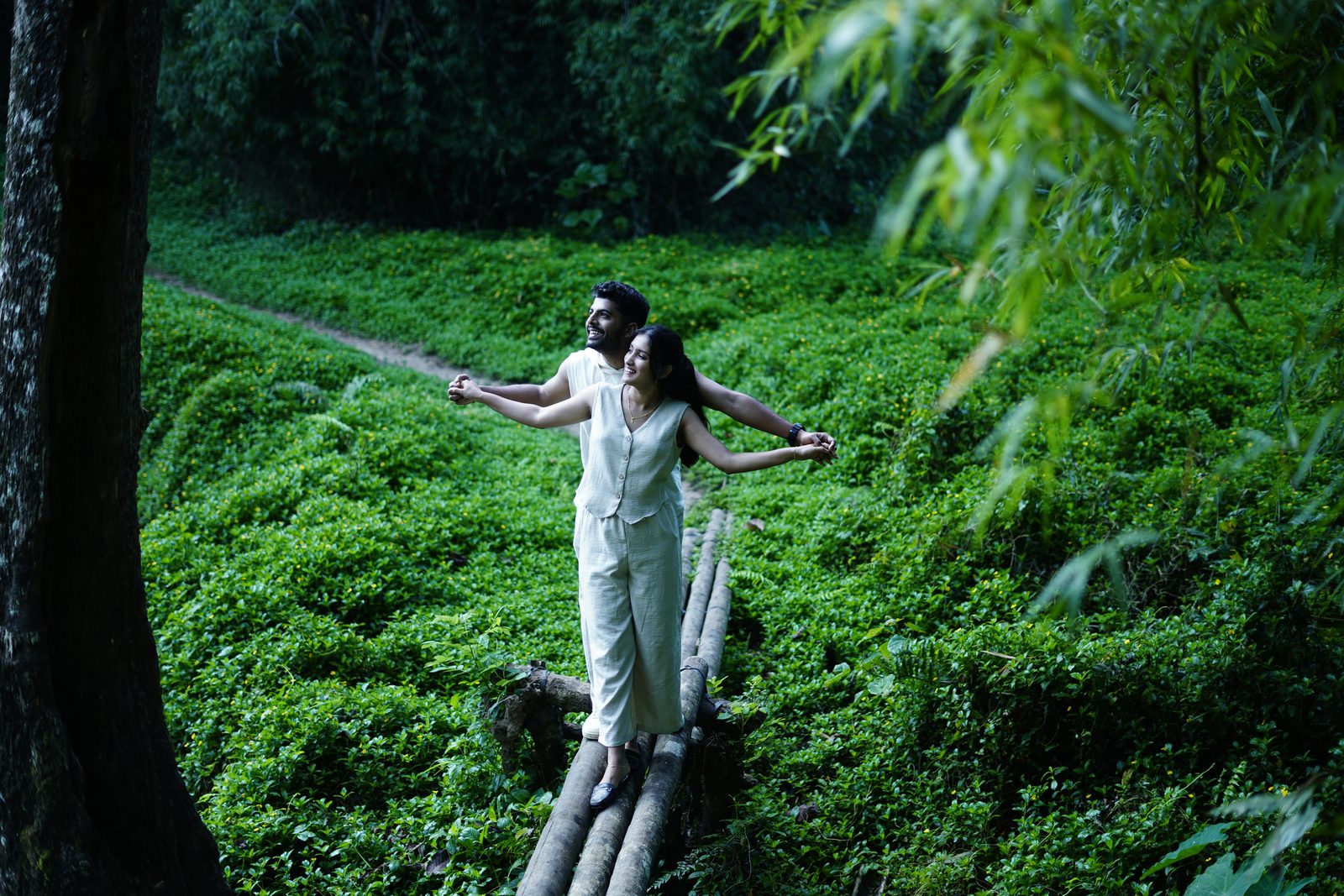 A woman balancing on a log with arms outstretched among green plants