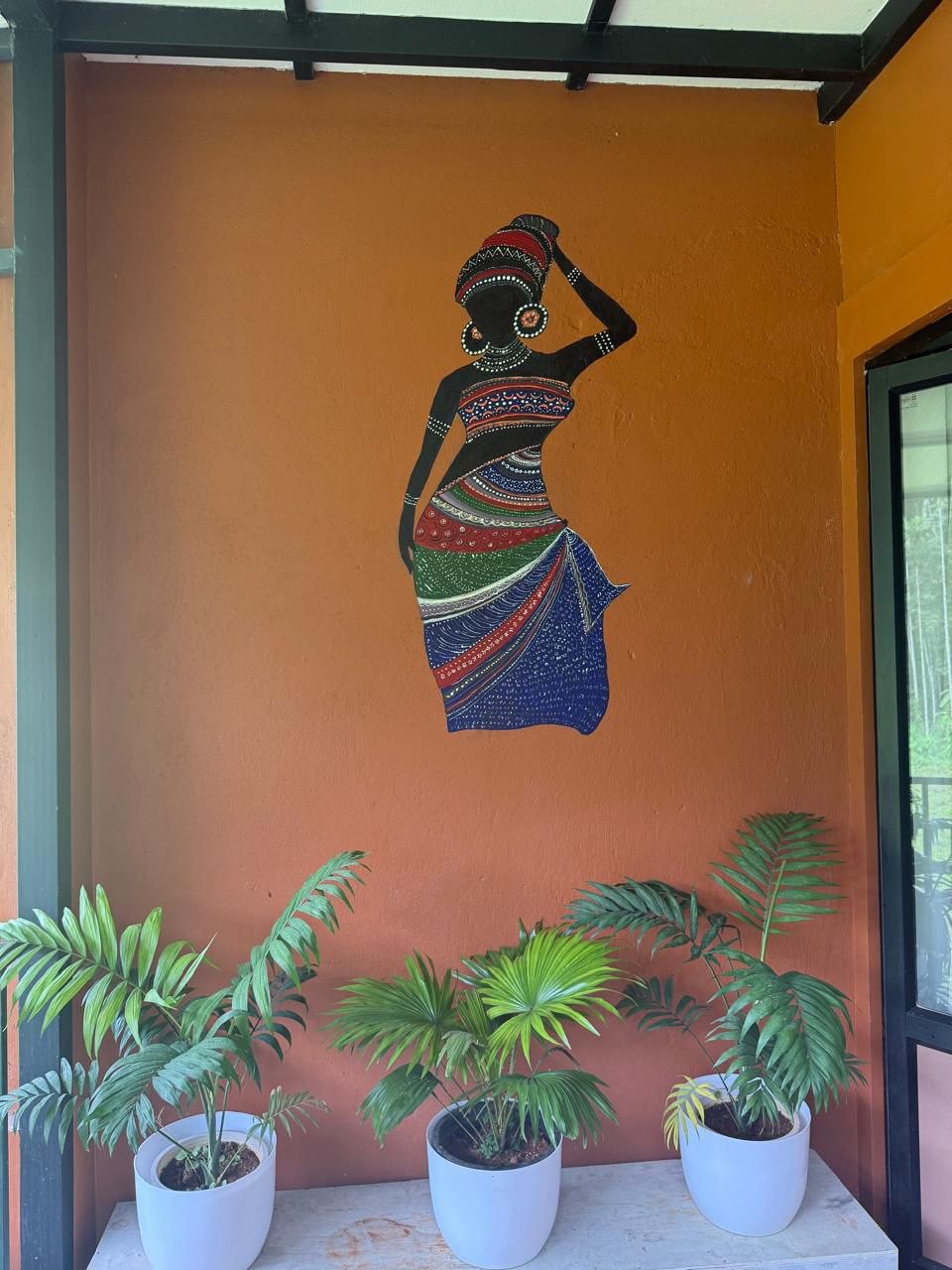Hand-painted mural of a figure carrying a pot on the terracotta veranda wall