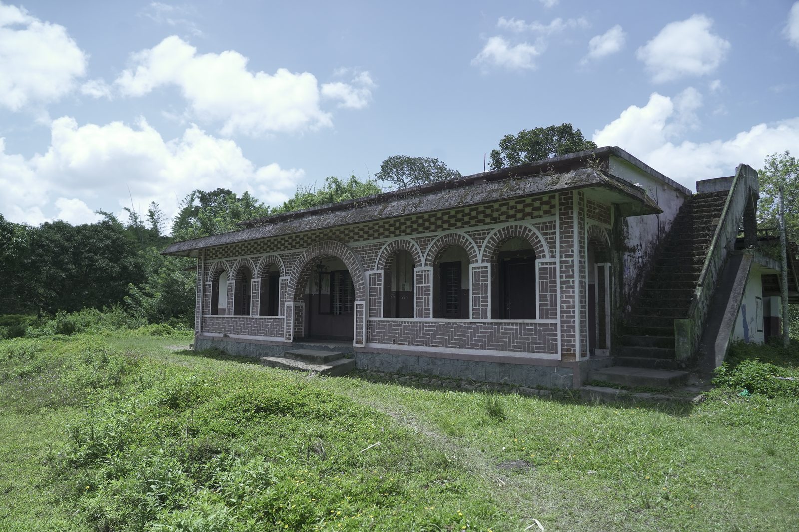 Old brick building with arched windows and an outside staircase in a grassy field