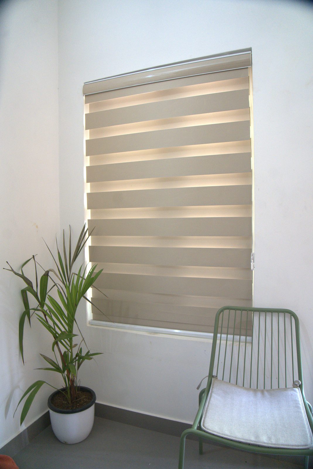 Window with layered blinds, a green chair and a potted plant