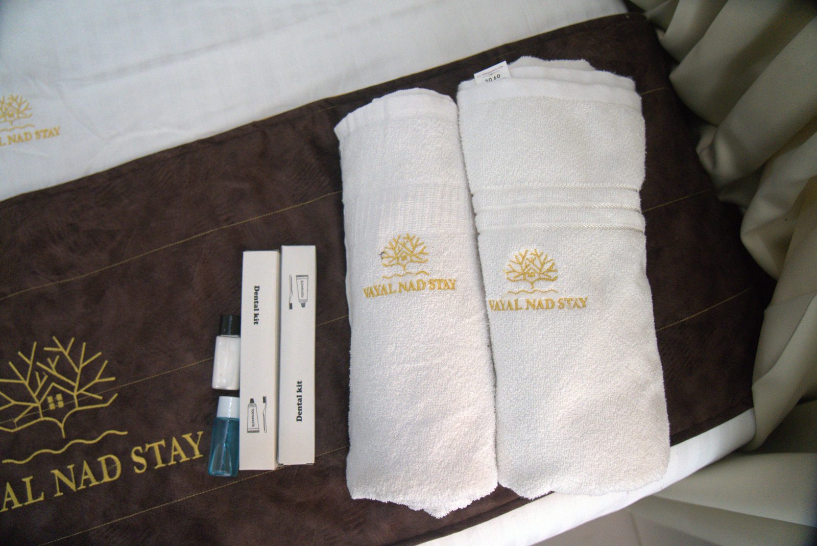 Folded towels and a dental kit on a branded bed runner