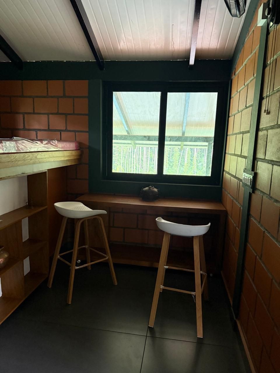 Two bar stools at a wooden ledge desk below a window with a forest view